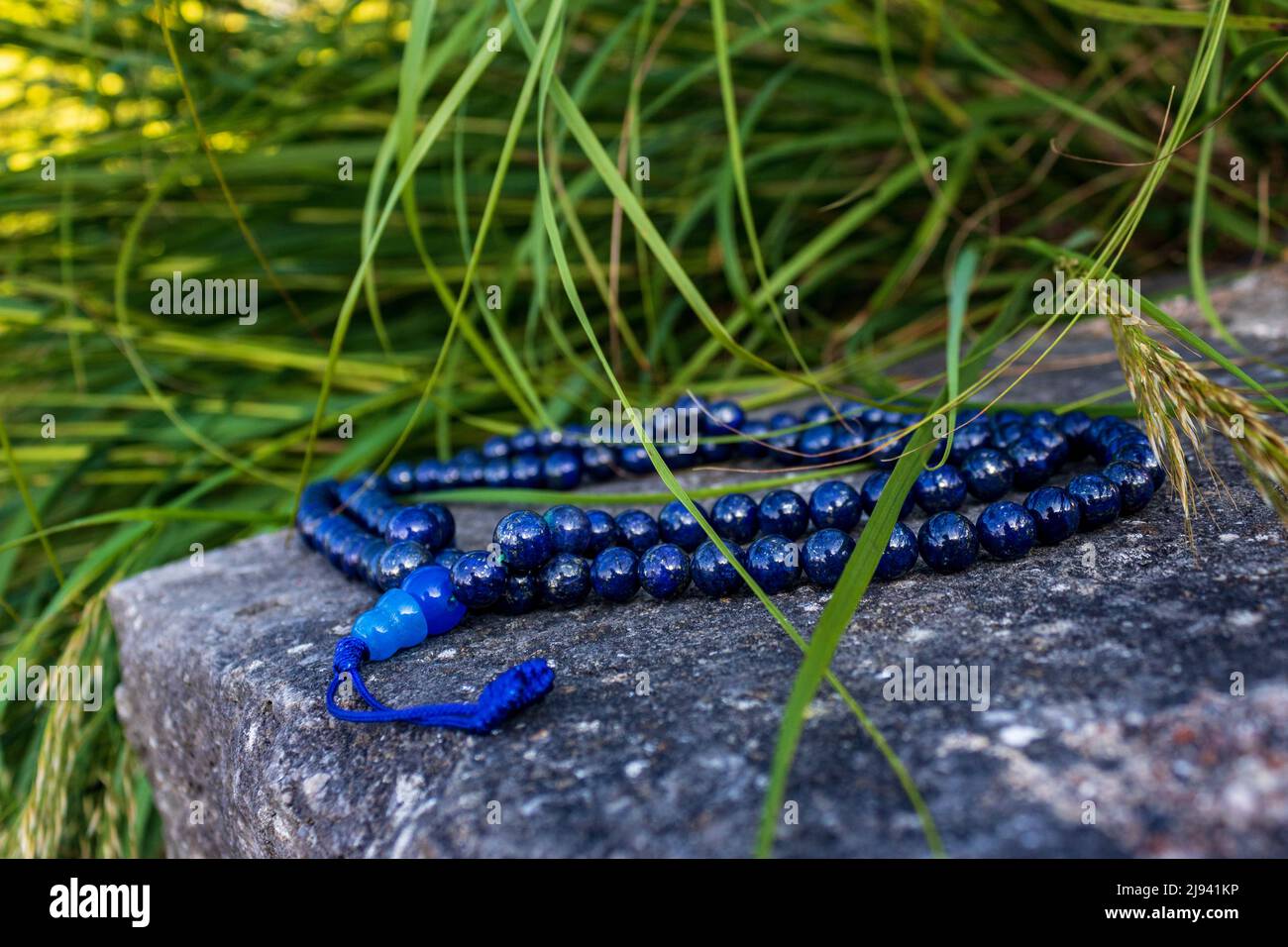 Blaue mala-Perlen oder buddhistische Gebetsperlen auf Felsen mit Gras in natürlicher Umgebung, Nahaufnahme und selektiver Fokus. Meditationszubehör Stockfoto