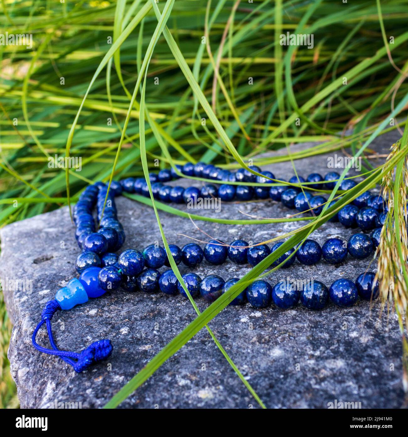 Blaue buddhistische Gebetsperlen für Mantra meditiaon, Nahaufnahme auf Felsen mit grünem Gras in der Natur. Spirituelles Zubehör Stockfoto