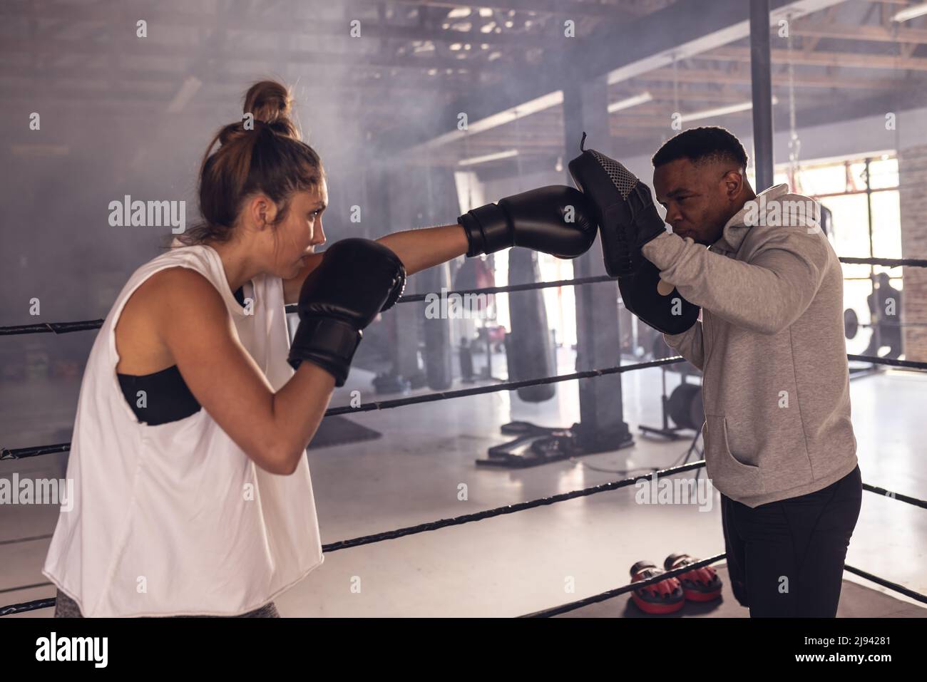 afroamerikanischer Trainer mit Boxerpfoten, der die kaukasische junge Boxerin trainiert Stockfoto