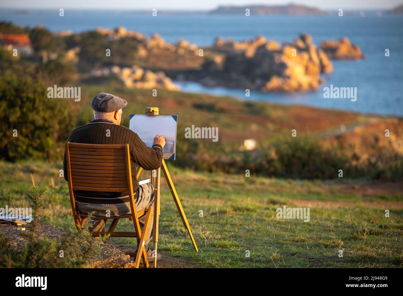 Ein Künstler, der Ploumanac'h und die rosaroten Felsen bei Sonnenaufgang malt, mit Sept Isles Beyond, Côtes-d'Armor, Bretagne, Frankreich Stockfoto