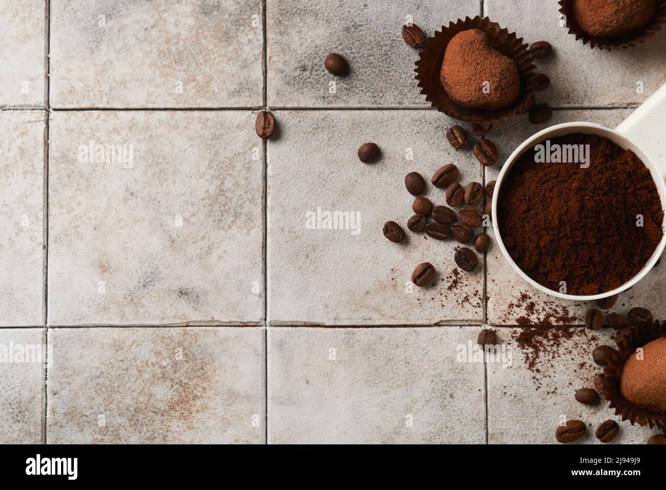 Hintergrund für Kaffee. Messlöffel mit gemahlenem Kaffee, Bohnen, Tasse und süßen Schokoladentrüffeln auf alten Kacheln geknackt Tischhintergrund. Hintergrund der Speisen. Stockfoto