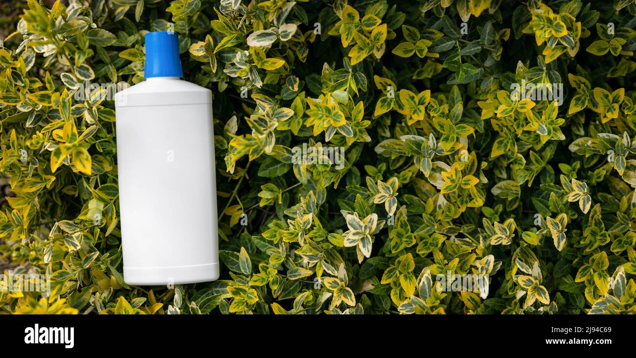 Leere Plastikdüngerflasche auf grünen Gartenpflanzen. Banner mit Kopierfläche Stockfoto