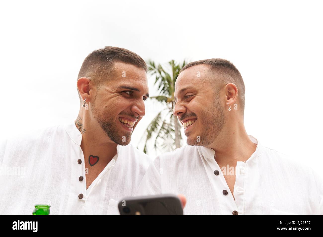 Schwule Paare, die sich zärtlich angussen, während sie das mobile im Freien benutzen Stockfoto