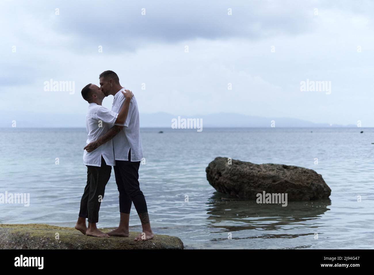 Homosexuelles Paar küsst sich auf einem Felsen mit Blick auf das Meer Stockfoto