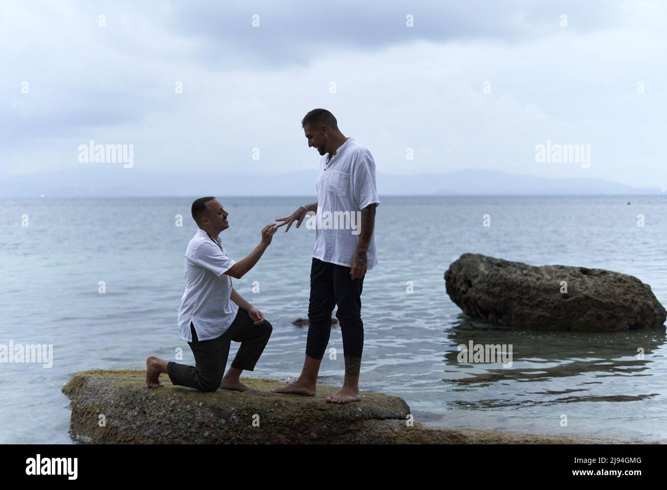 Schwuler Mann auf den Knien, der seinen Partner bittet, ihn am Meer zu heiraten Stockfoto