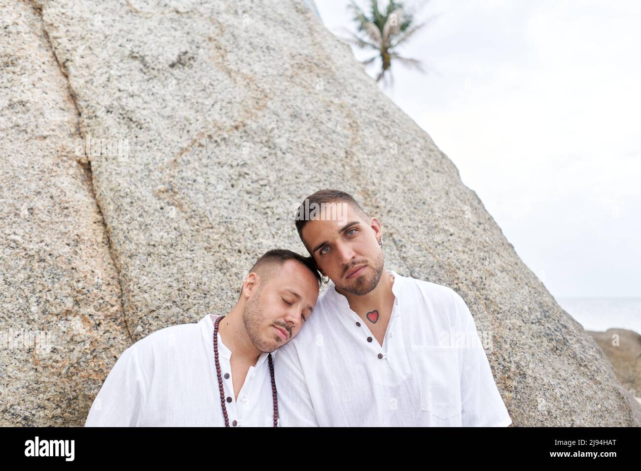 Gay Mann lehnte seinen Kopf auf die Schulter seines Paares, während er auf einem Strand stand Stockfoto