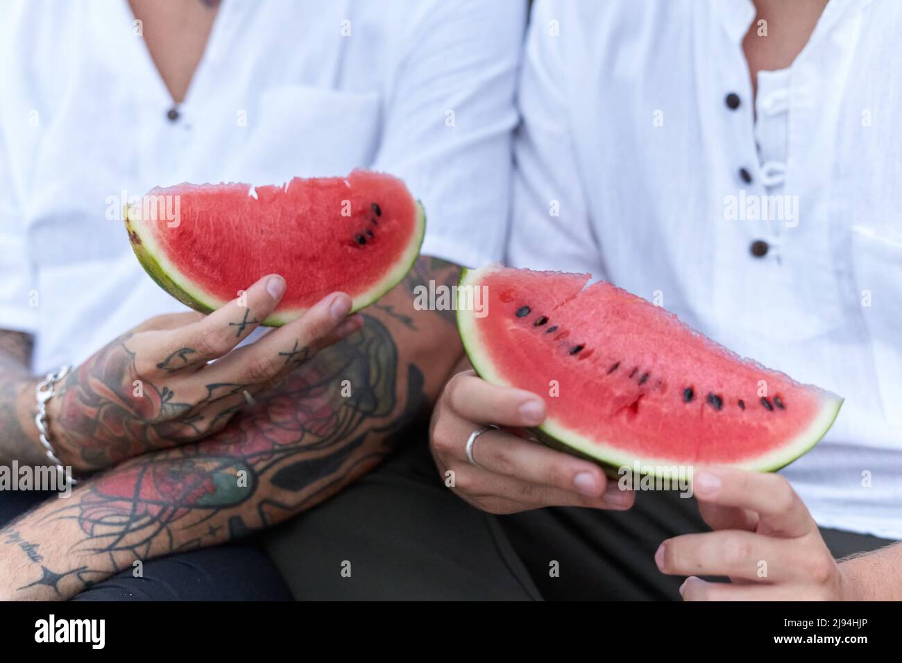 Hände von zwei Männern, die ein Stück Wassermelone am Strand halten Stockfoto