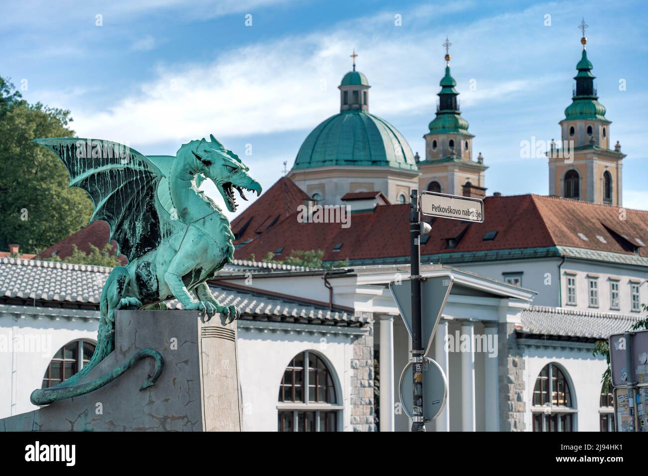 Ljubljana, Slowenien - 07.15.2021: Bronzeskulptur des Drachen mit blauem Himmel und Kathedralenhintergrund, Blick nach rechts Stockfoto