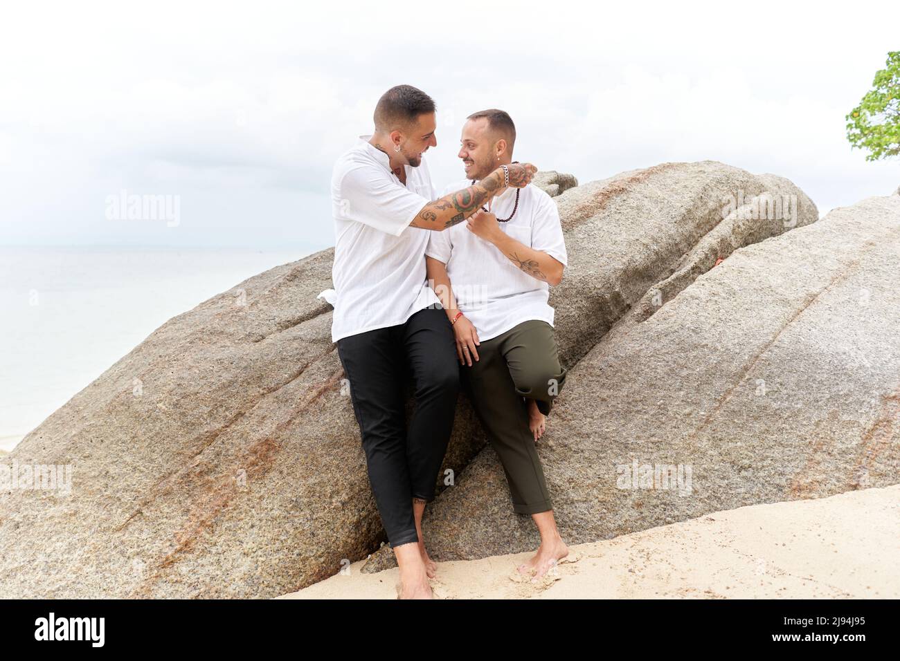 Homosexueller Mann, der seinem Partner an einem tropischen Strand eine Kugelkette gibt Stockfoto