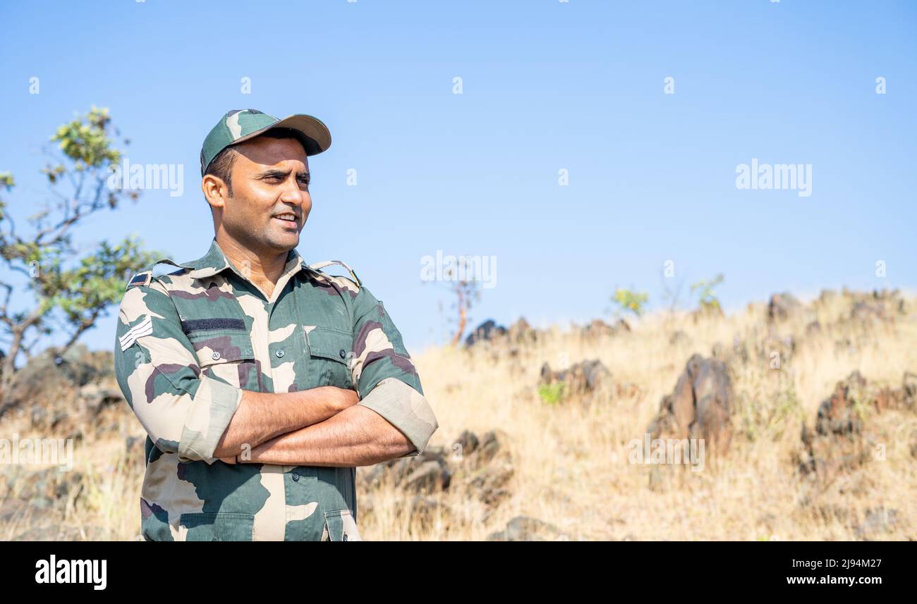 Glücklich lächelnder indischer Soldat, der mit gekreuzten Armen und Blick auf die Kamera steht - Konzept von selbstbewusst, furchtlos und im Dienst. Stockfoto