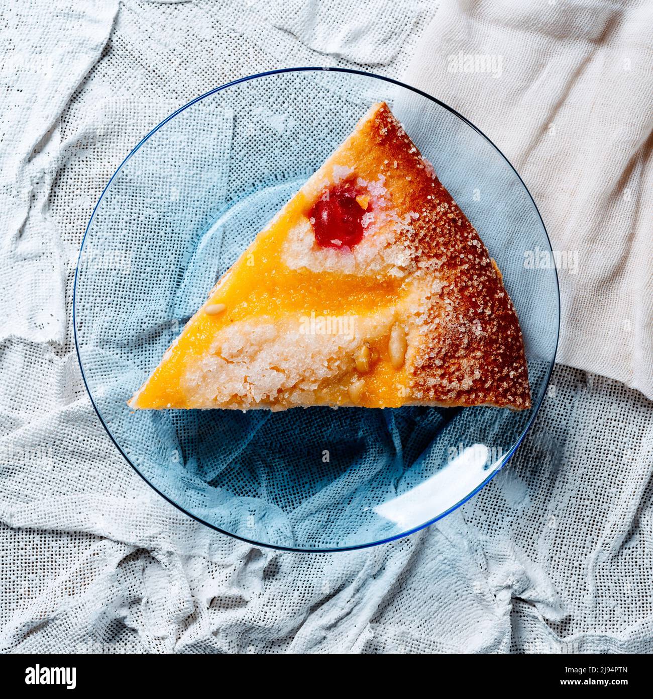 Blick aus der Perspektive auf ein Stück Coca de sant joan, eine typische süße flache Torte aus katalonien, spanien, gegessen am saint johns Eve, serviert in einem blauen Glas pla Stockfoto