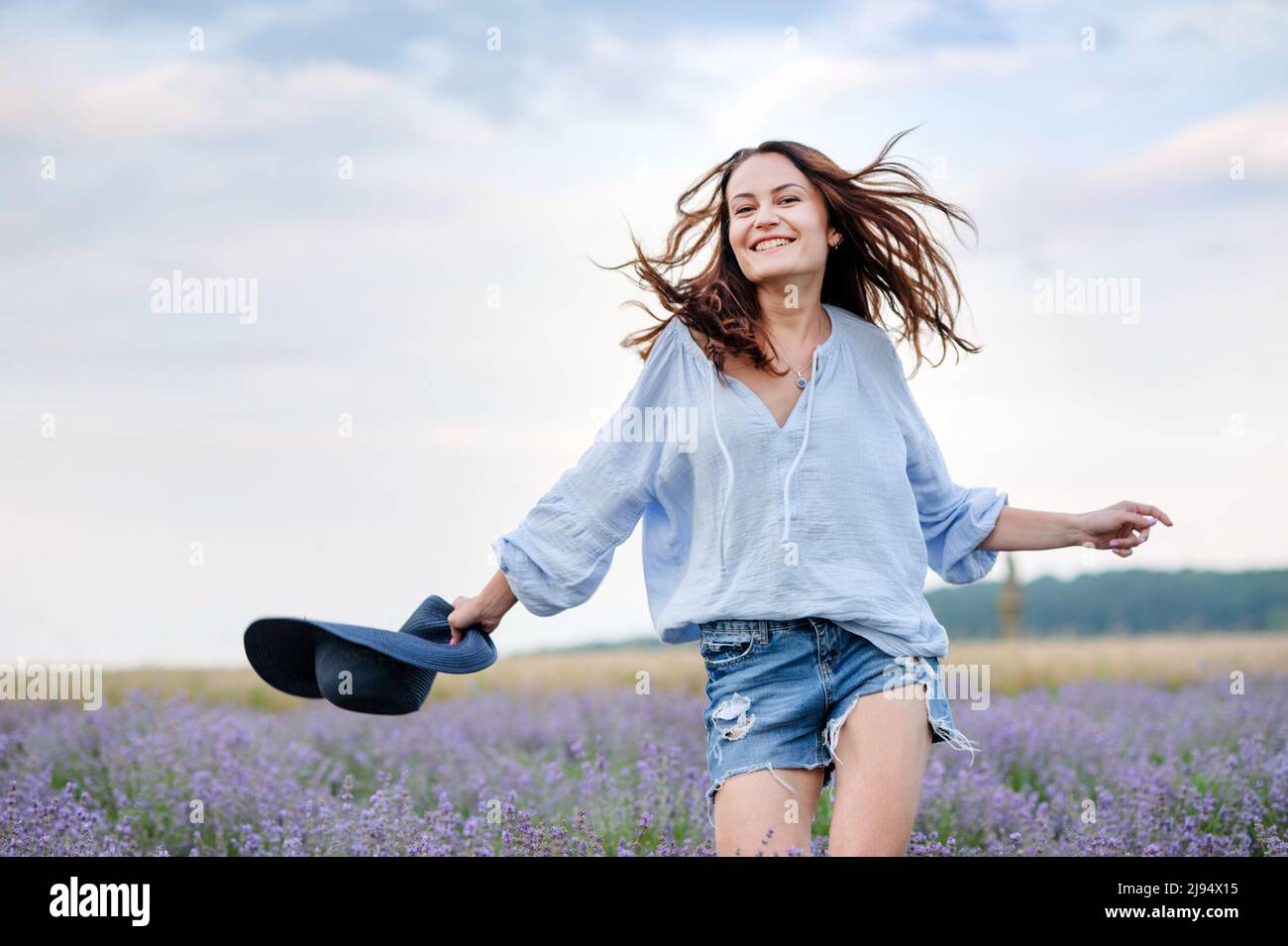 Glückliches Mädchen, das im Lavendelfeld läuft und Hut in der Hand hält, flatterndes Haar Stockfoto