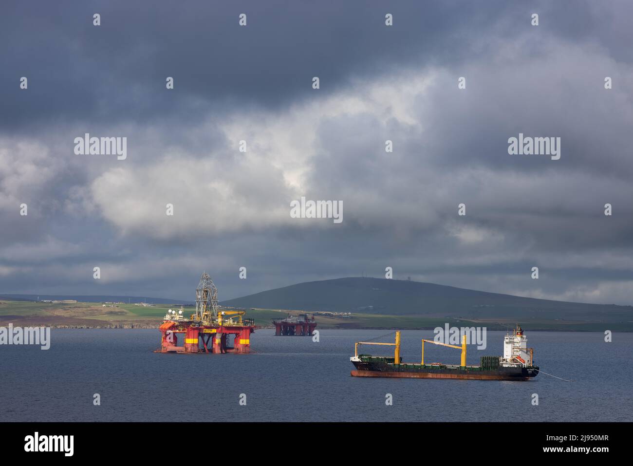 Ein Massengutfrachter und Ölförderanlagen in Scapa Flow, Orkney Isles, Schottland, Großbritannien Stockfoto