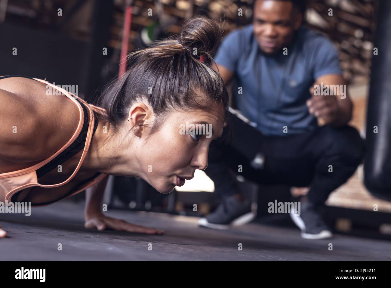 afroamerikanischer junger Trainer führt kaukasische junge Boxerin mit Liegestützen im Fitnessclub Stockfoto