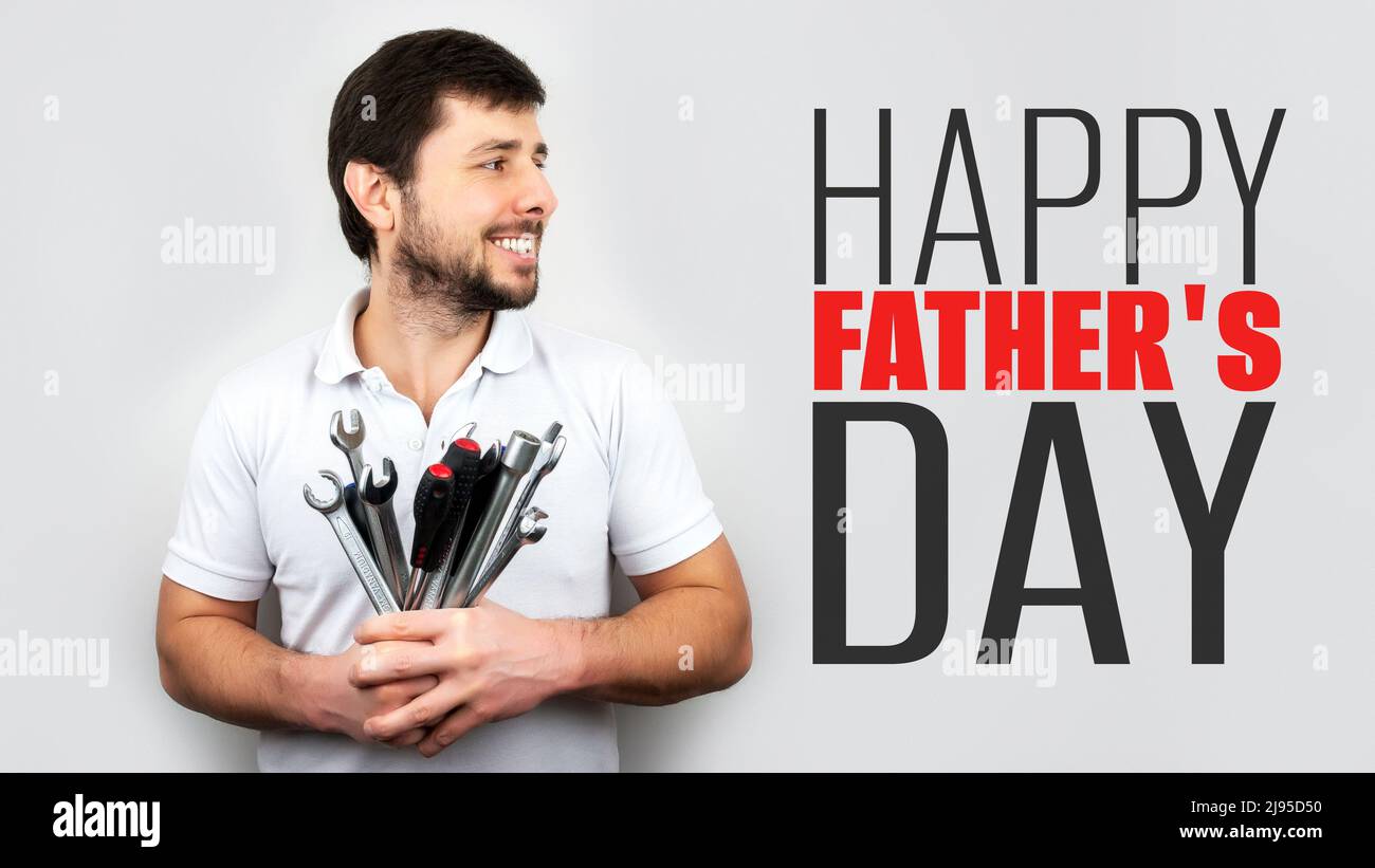 Lächelnder, glücklicher bärtiger Mann mit einem Strauß Schraubenschlüssel, Schraubenschlüsseln und Schraubendrehern mit Inschrift Happy Father's Day. Happy Fathers Day Konzept oder Greeti Stockfoto