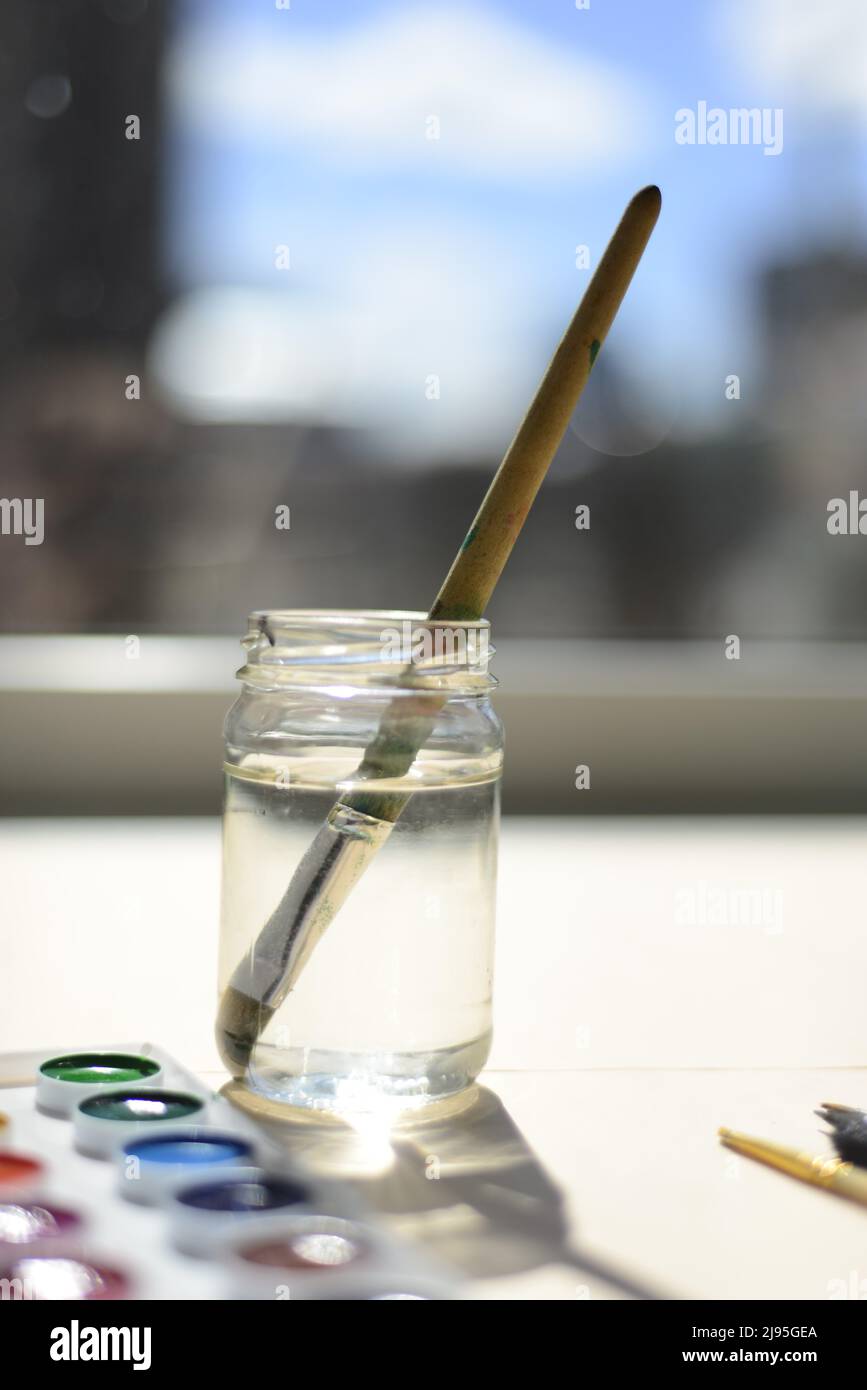 Auf dem Fenster steht ein Glas mit Wasser und einer Bürste. Neben den Aquarellen. Zeichenstunde. Stockfoto