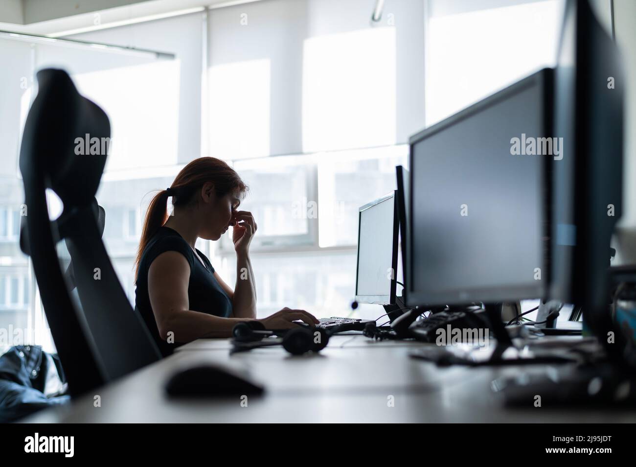 Müde Frau workaholic T-Shirt arbeitet in einem leeren Büro und hält die Finger auf dem Brücke der Nase. Ein Mädchen mit Kopfschmerzen arbeitet Überstunden. Weiblich Stockfoto