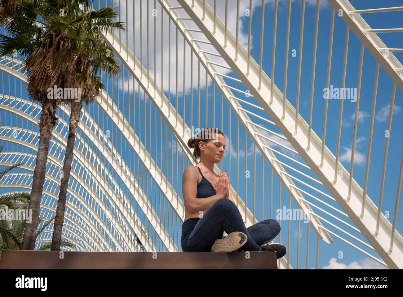 Fit Frau praktiziert Yoga und meditieren draußen, moderne Architektur und Palmenhintergrund. Stockfoto