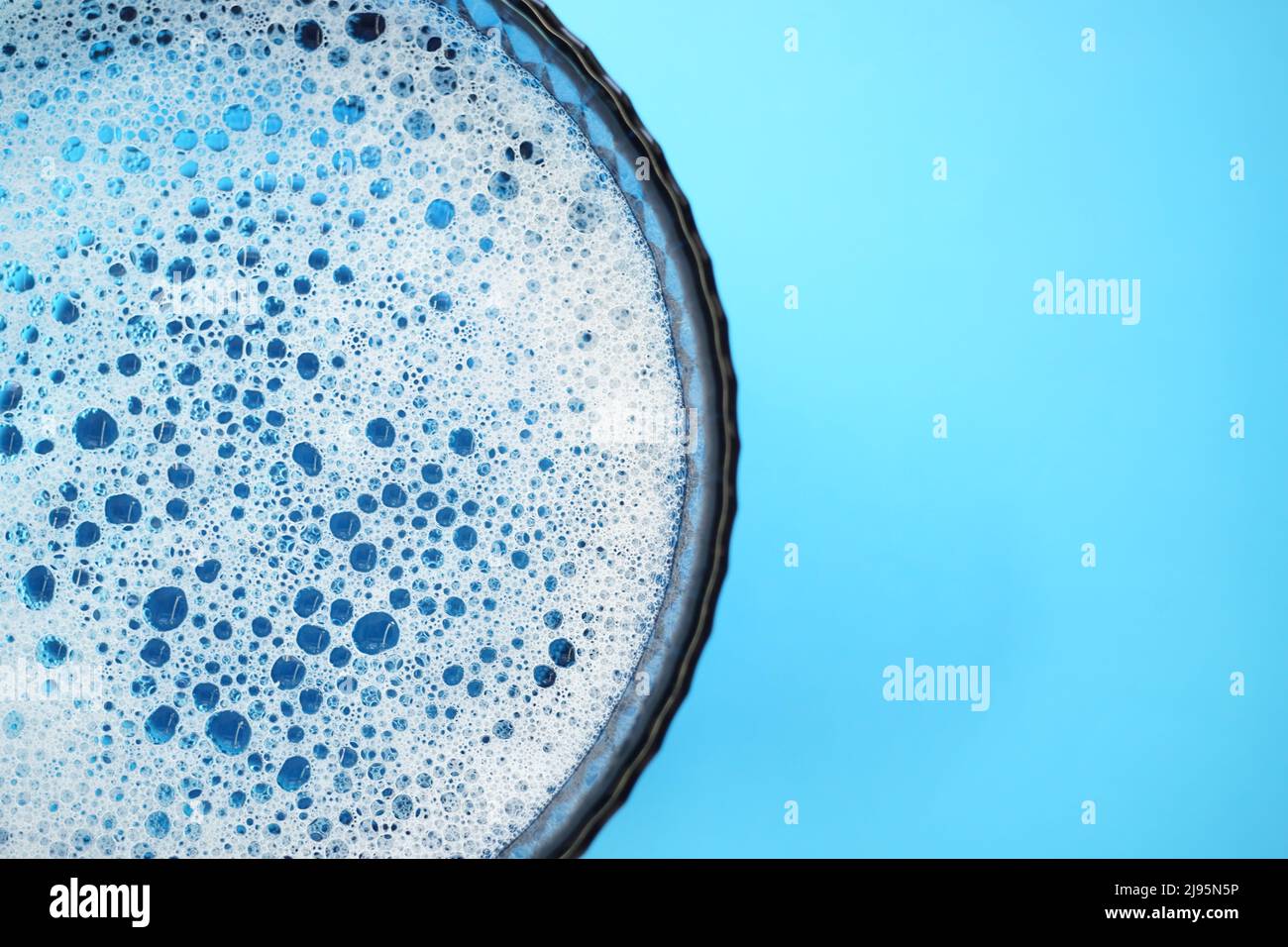 Glasschale mit schaumigem Wasser und Blasen, die auf einem blauen Tisch platzen, Platz kopieren. Stockfoto