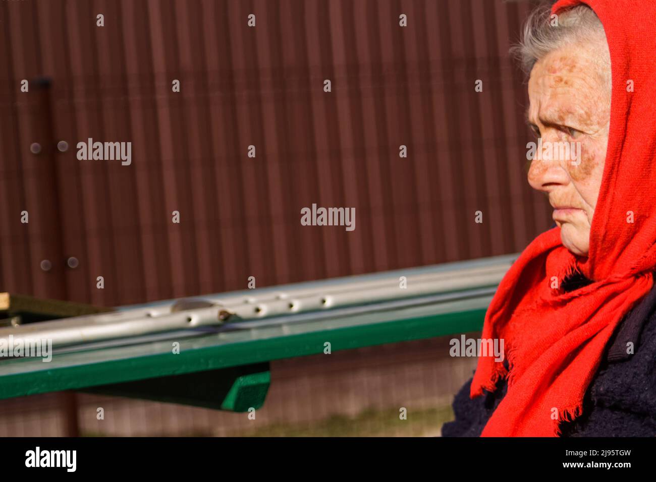 Defokussieren sie die ältere ukrainische Frau in einem roten Schal mit Krücken, die draußen sitzen. Frau 85 Jahre alt. Einzelperson. Nahaufnahme. Krank und heimatverbunden. Traurig Stockfoto