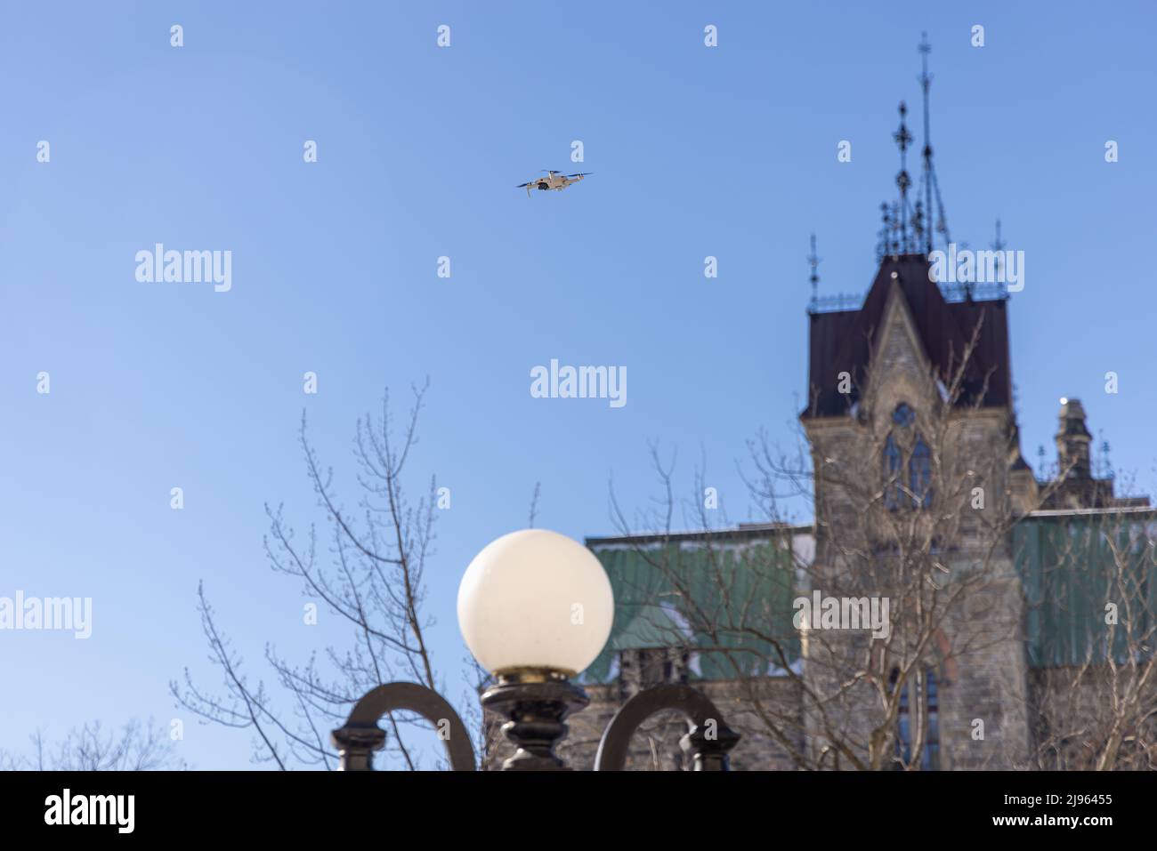 Eine Drohne fliegt hoch über einem klaren blauen Himmel mit verschwommenen Stadtgebäuden im Hintergrund, die zunehmend als Überwachung genutzt werden. Mit Kopierbereich. Stockfoto