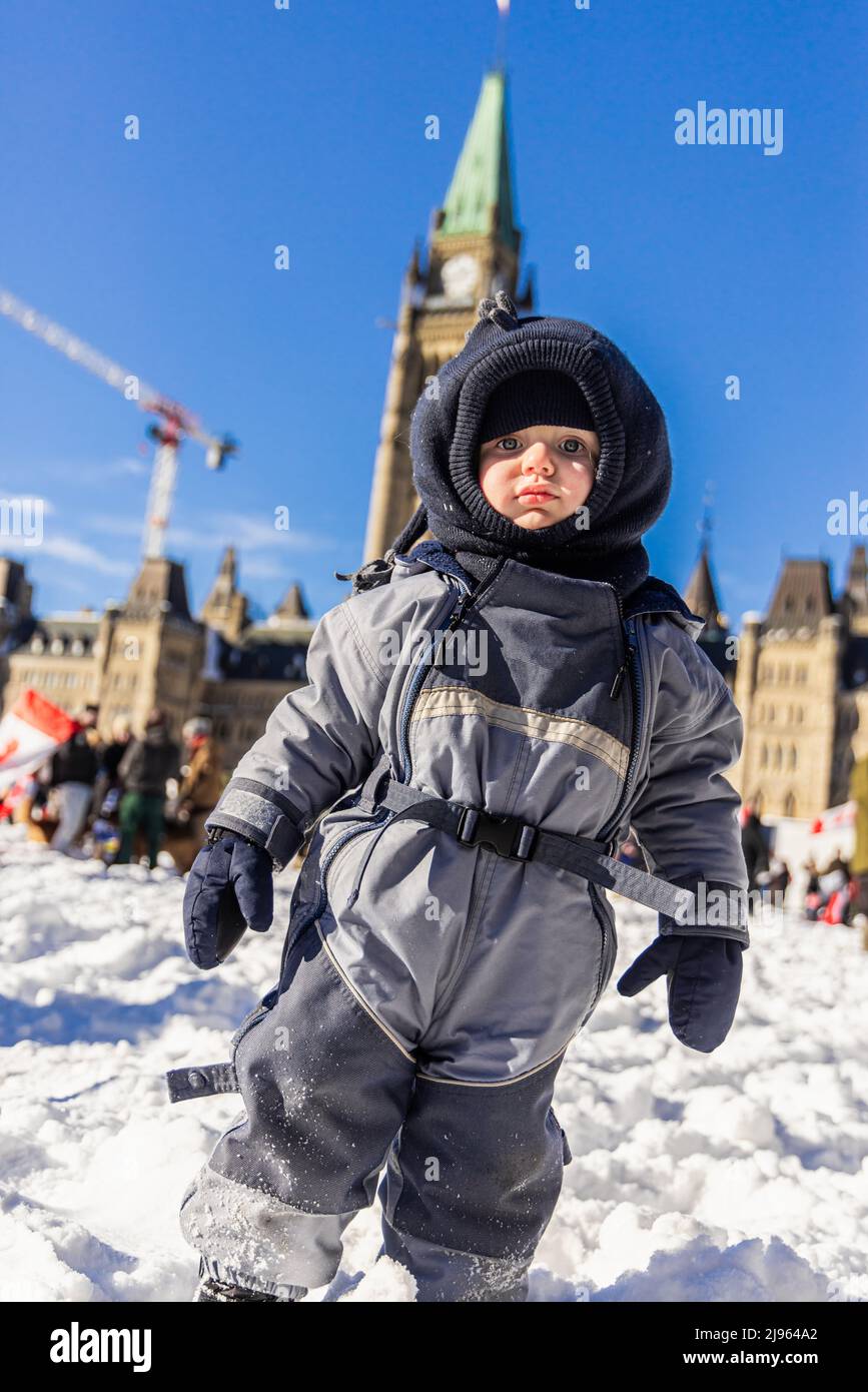 Porträt eines niedlichen dreijährigen Jungen, der vor dem Parlament von Ottawa steht, mit verschwommenem Hintergrund an einem hellen Wintertag mit Kopierfläche. Stockfoto