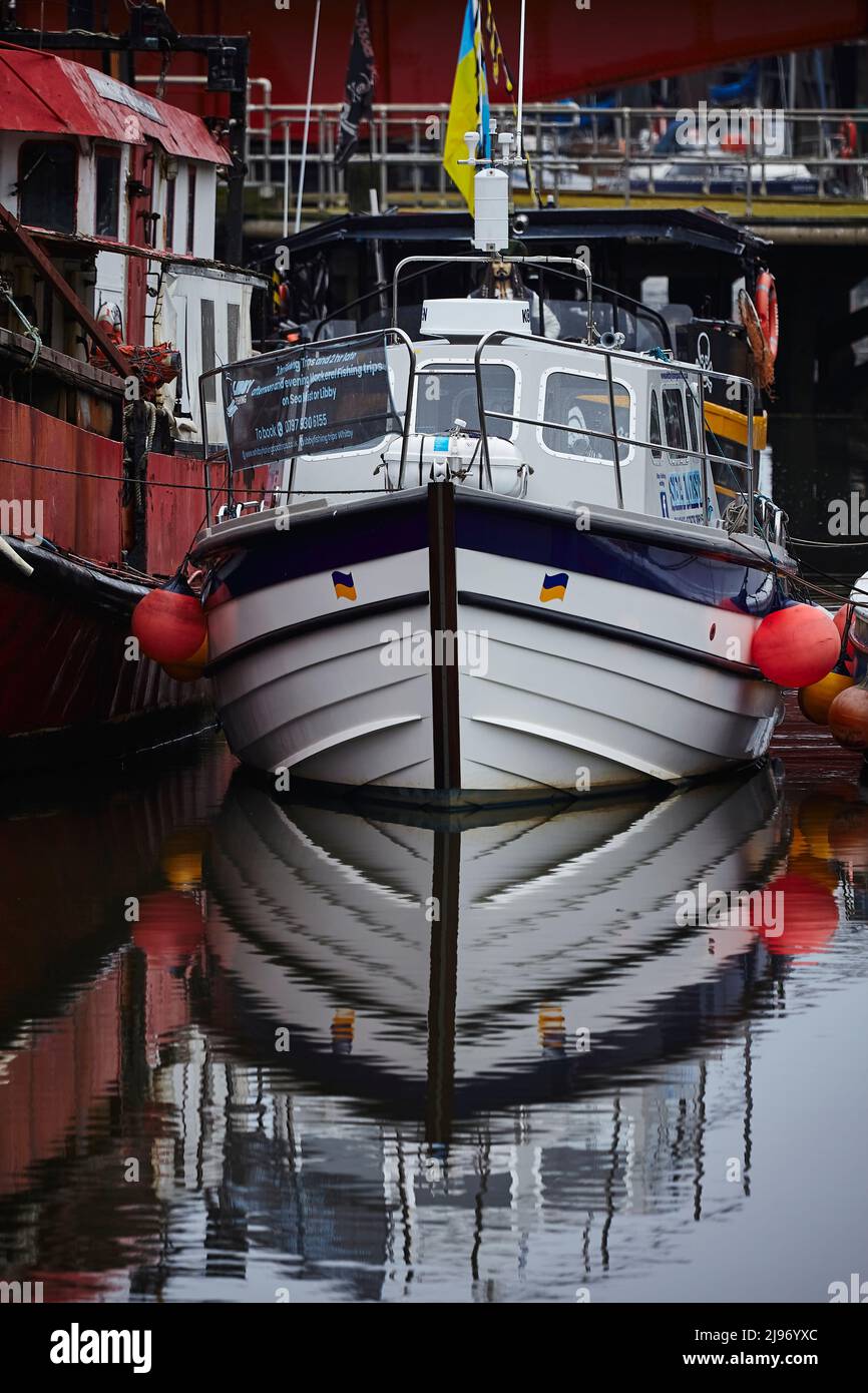 Festgetäutes Ausflugsboot mit ukrainischer Flagge und Wasserspiegelungen. Whitby 16052022 Stockfoto