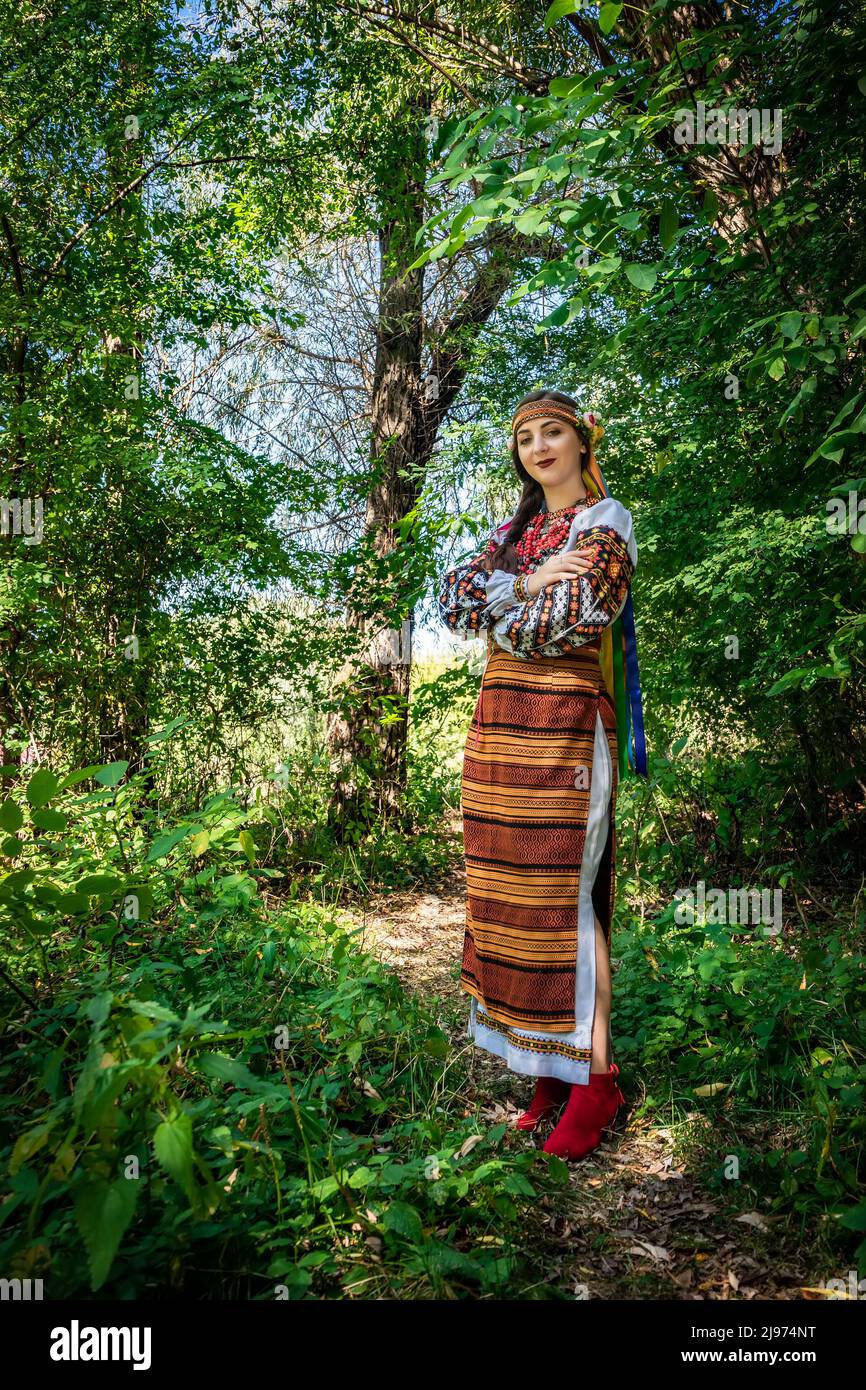 Ukrainisches Mädchen in ukrainischer Nationaltracht steht auf einem Pfad im Wald. Stockfoto