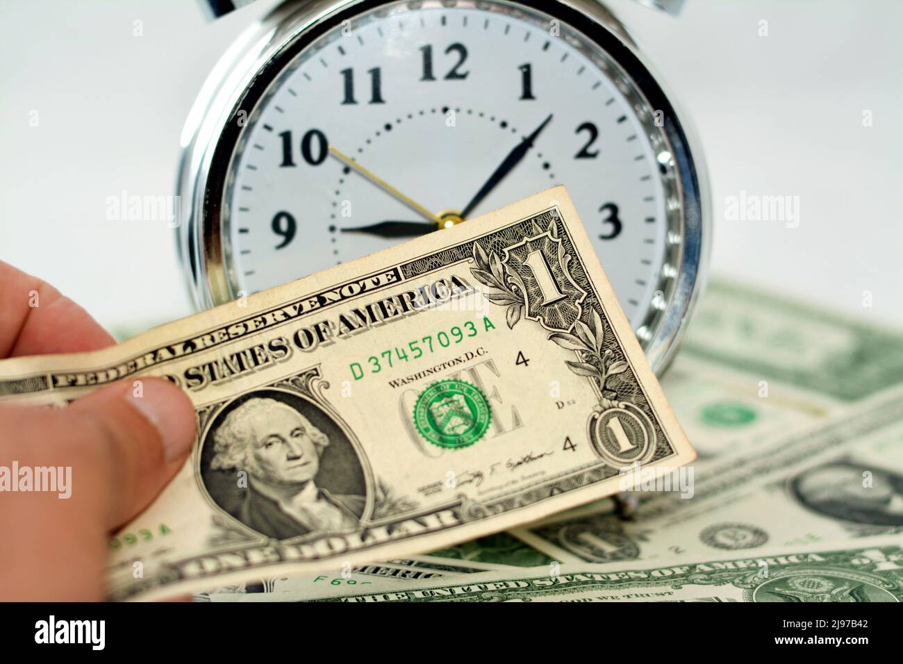 Zahlen Sie amerikanische Geldscheine, US-Dollar mit einem verschwommenen Wecker-Timer in Stunden, Minuten und Sekunden Skala im Hintergrund, zahlen Sie Stockfoto