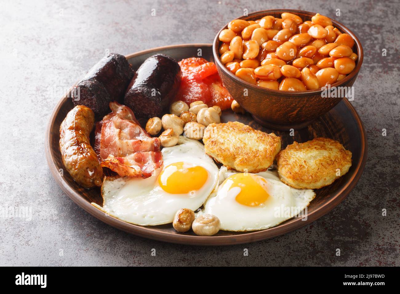 Komplettes englisches Frühstück mit Spiegeleiern, Würstchen, Speck, Blutwurst, Bohnen, Tomate in der Nähe in der Platte auf dem Tisch. Horizontal Stockfoto