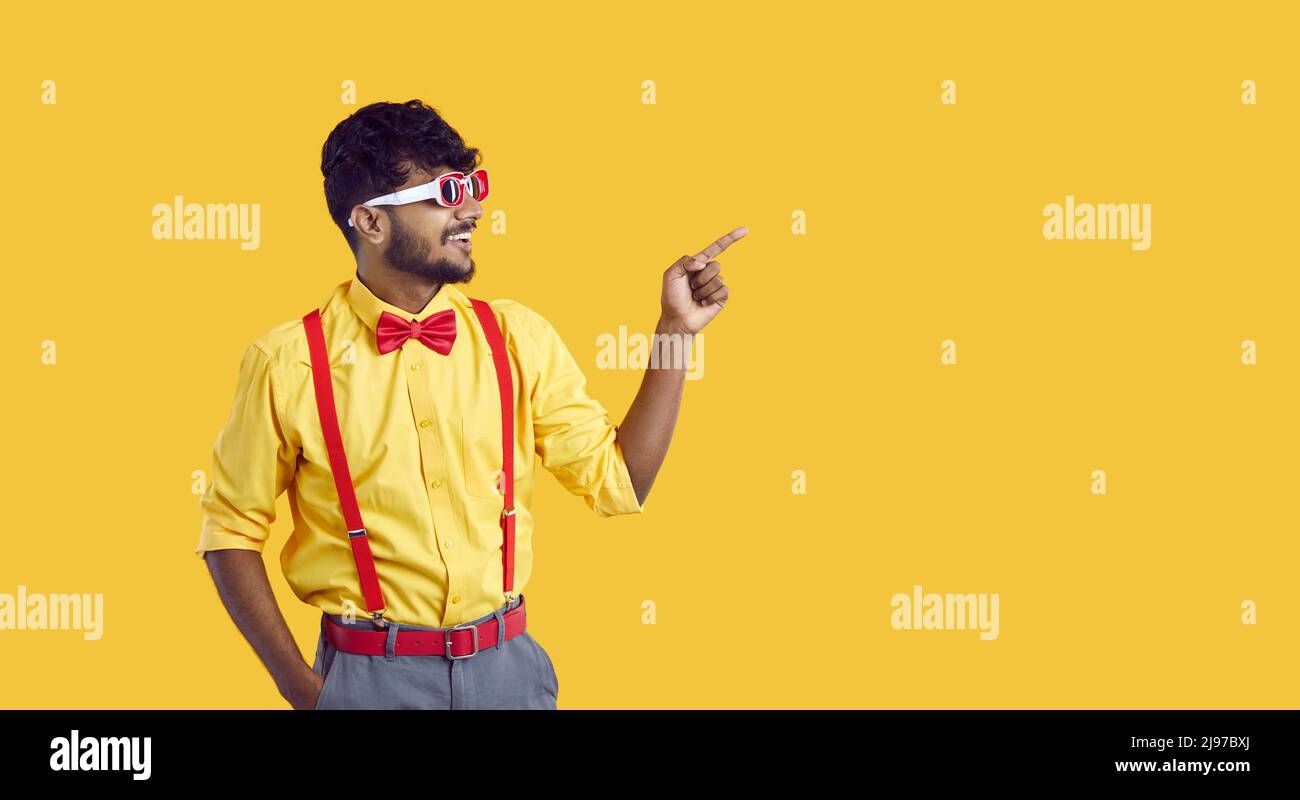 Glücklicher junger indischer Mann zeigt auf Seite, um etwas auf gelbem Kopierraum-Hintergrund zu zeigen Stockfoto
