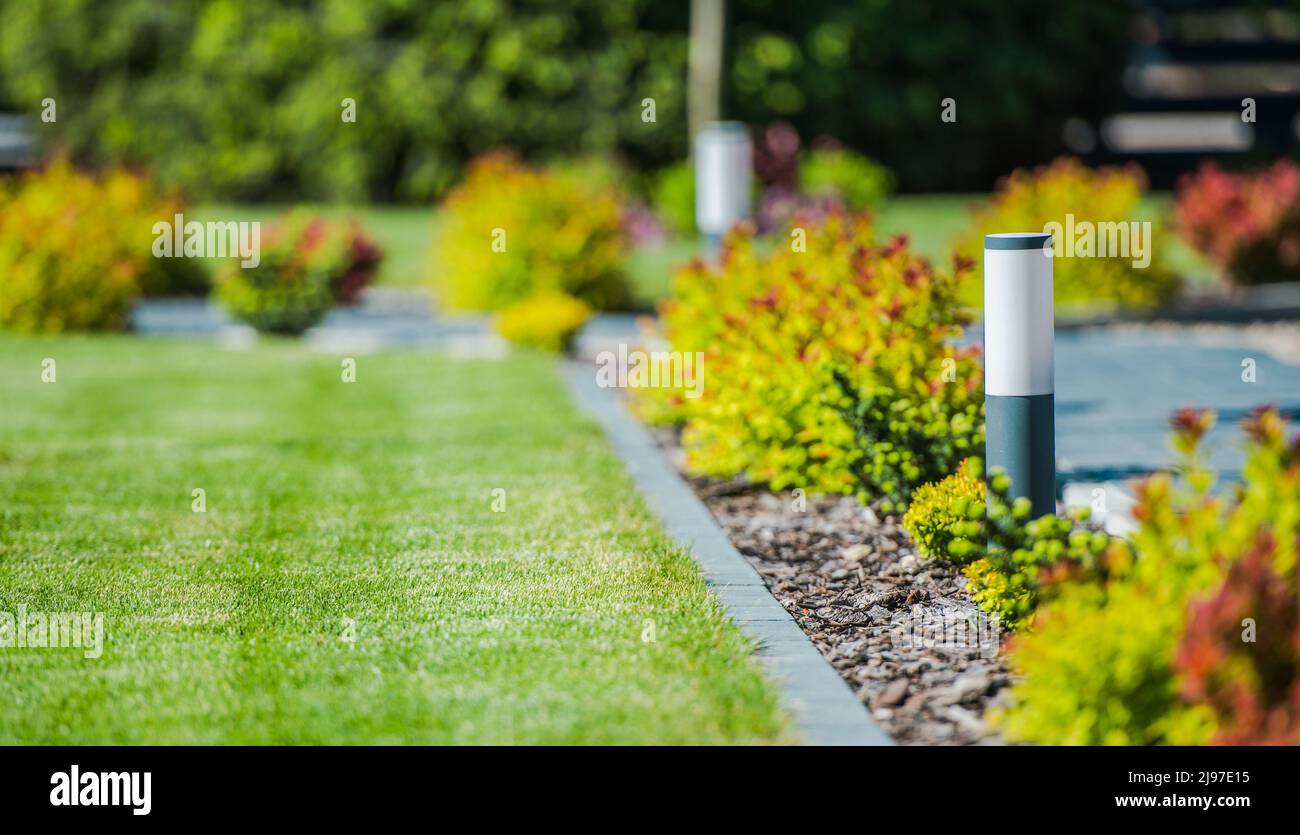 Moderner Garten mit dekorativer LED-Beleuchtung im Garten entlang eines Pfades und einer Rasenfläche auf der anderen Seite. Wohngebiet Landschaftsthema. Stockfoto