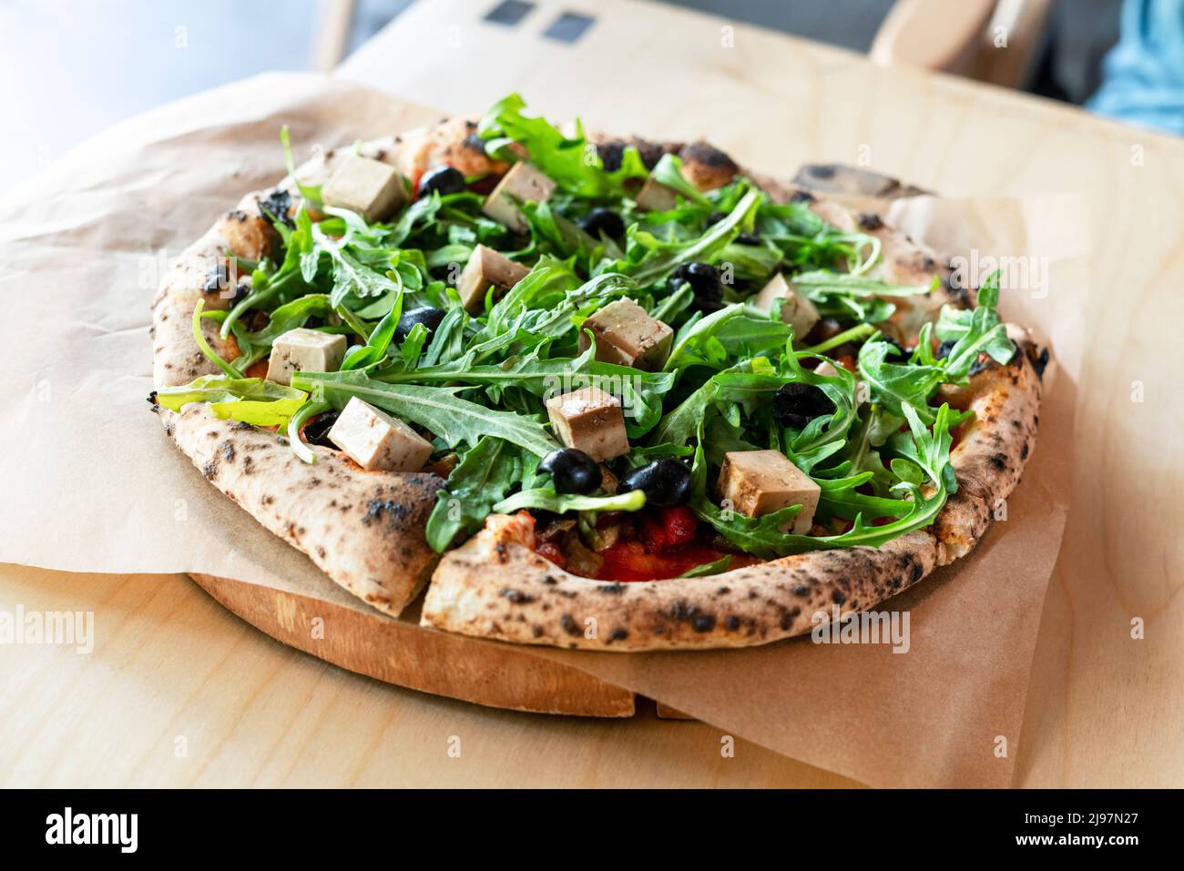 Draufsicht auf vegane Pizza mit Rucola oder Rucola Tofu Oliven und Tomaten Nahaufnahme Holzbrett Vegetarisches Essen gesunde Ernährung selektiver Fokus Stockfoto