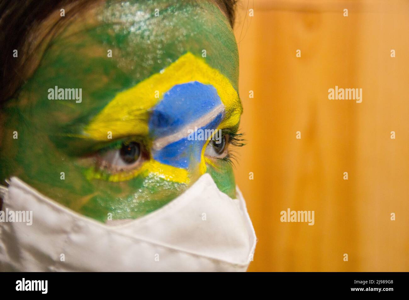 Kind mit einer Maske, dessen Gesicht mit der Flagge Brasiliens bemalt ist. Stockfoto