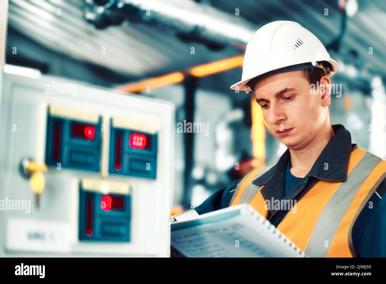 Ein Industrieingenieur im Helm überprüft oder justiert Geräte in einer Gasverarbeitungsanlage oder -Anlage. Authentischer Szenenablauf. Stockfoto