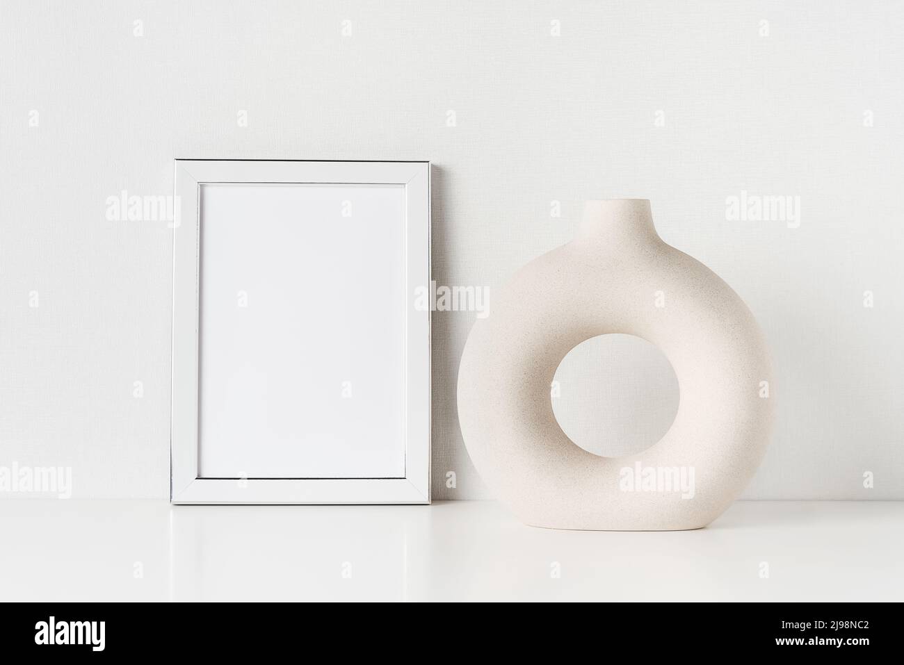 Weißer Rahmen-Mockup und runde Keramikvase auf einem weißen Tisch an der Wand. Platz für Text kopieren Stockfoto