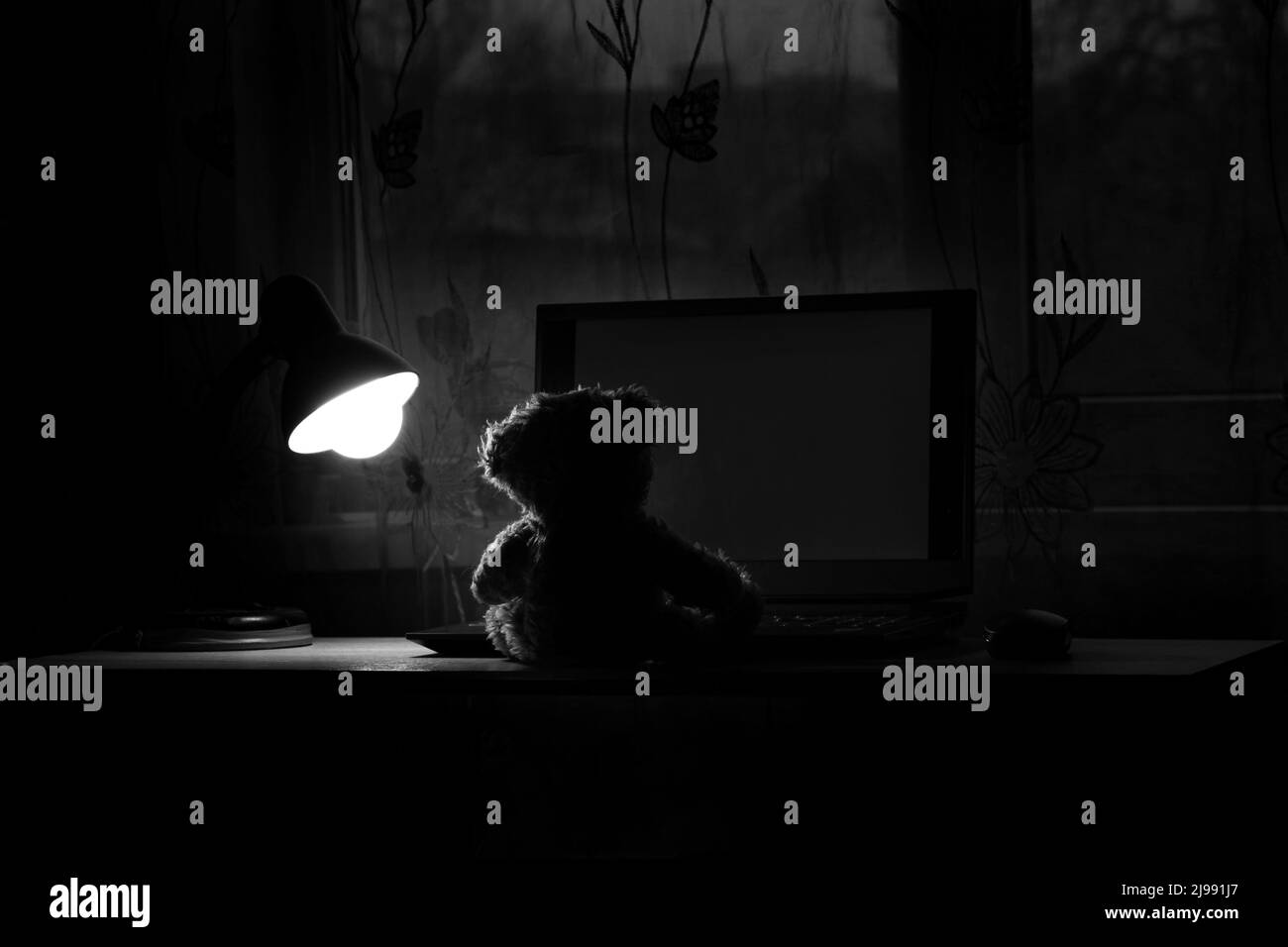 teddybär für Kinder sitzt mit einem Laptop auf dem Tisch, trägt nachts eine Tischlampe in den Schlafzimmern, trägt Fenster, Einsamkeit, Freude in a la Stockfoto