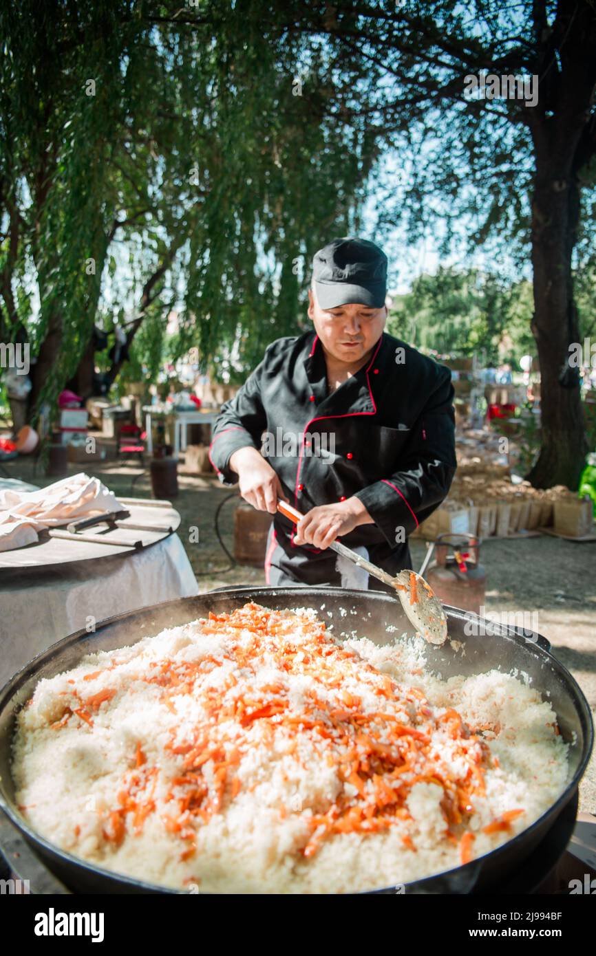 Ein männlicher Koch kocht Pilaf in einem großen Kessel auf der Straße. Stockfoto