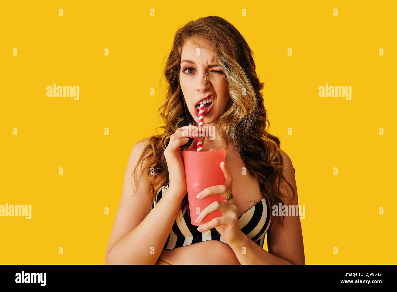 Ausdrucksstarke junge Erwachsene Frau, die Eiskaffee trinkt und Strohcocktail auf gelbem Hintergrund im Sommerstudio trinkt Stockfoto