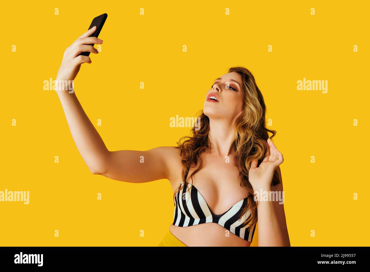 Porträt der schönen jungen Frau SMS flirt Selfie Foto-Nachricht mit Smartphone auf gelbem Hintergrund Studio Stockfoto