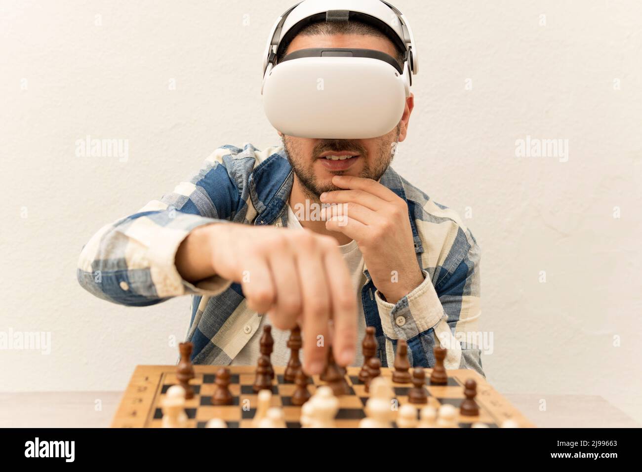 Nachdenklicher Mann, der in seinem Haus Online-Schach auf seiner Virtual-Reality-Brille spielt Stockfoto
