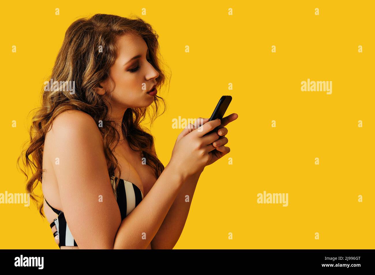 Portrait der schönen jungen Frau SMS flirt Nachricht mit Smartphone auf gelbem Hintergrund Studio Stockfoto