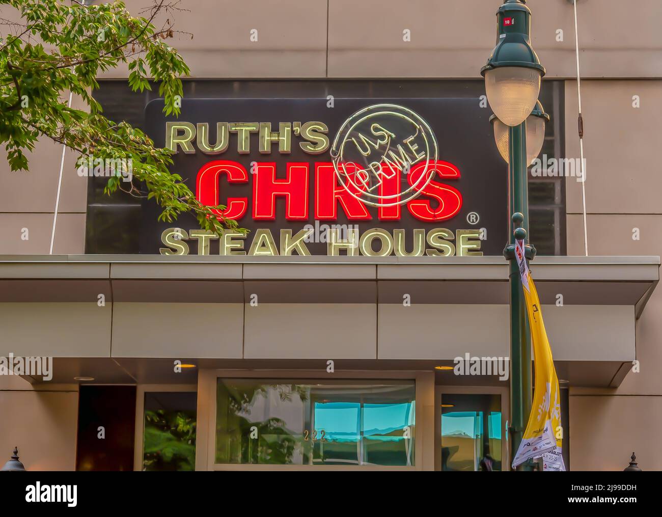 Horizontale Außenfassade mit Marken- und Logo-Beschilderung für das „Ruth's Chris“ Steak House im weichen Licht von Baumzweigen, Laternenpfosten und beleuchteten Neonröhren. Stockfoto