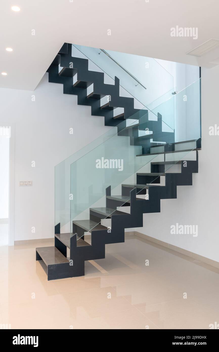 Eine moderne Treppe. Durchbrochene Treppen aus Metall und Marmor sowie gläserne Geländer. Stockfoto