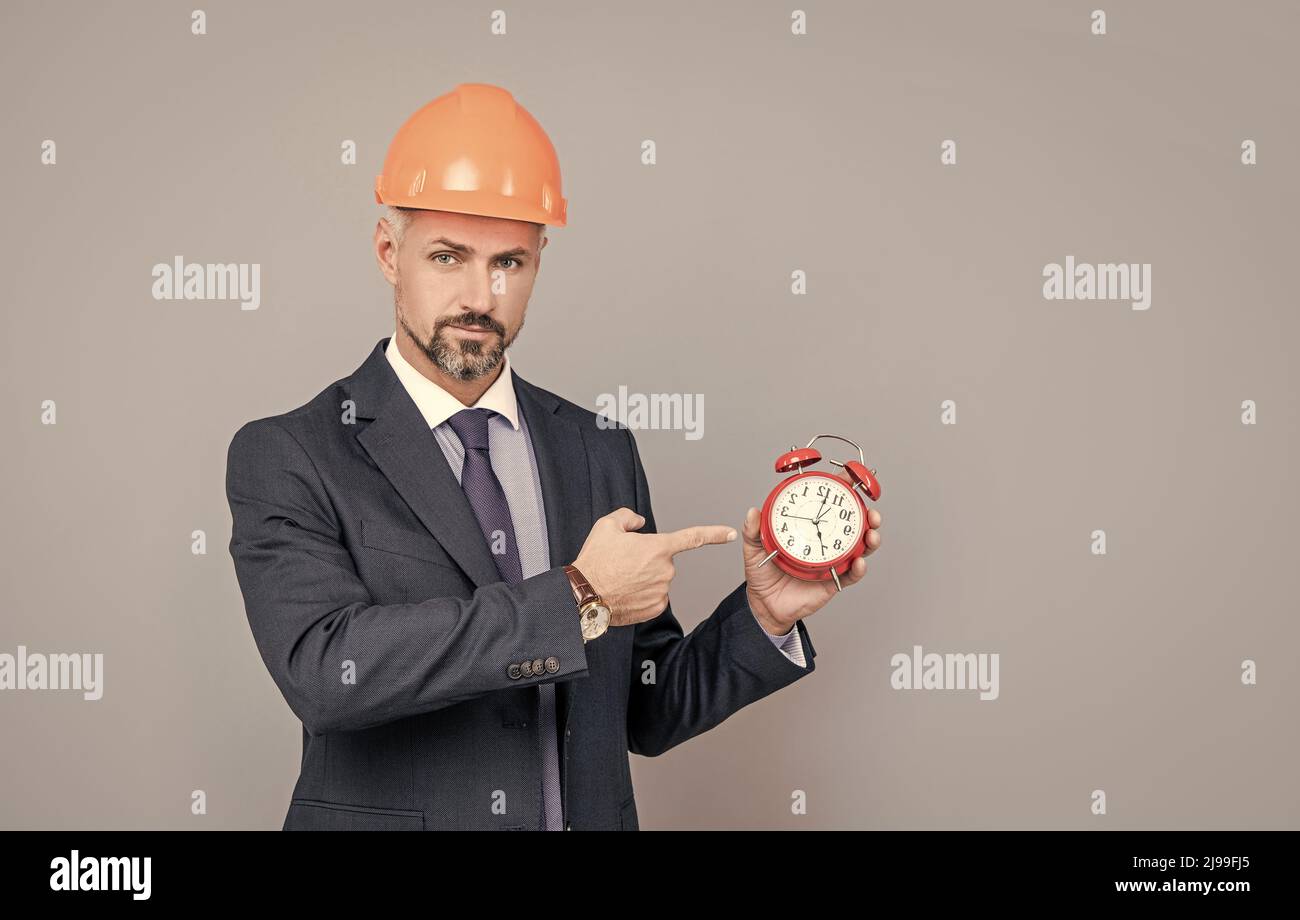 Geschäftsmann Ingenieur in Geschäftsanzug und Helm mit Wecker, kopieren Raum, Zeit Stockfoto