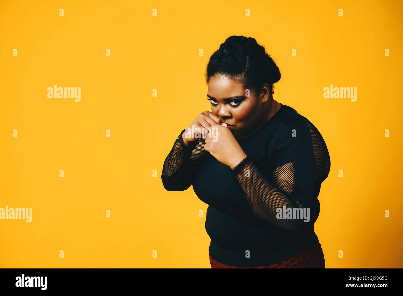 Porträt einer schwarzen Frau mit Armen in Kampfposition auf gelbem Hintergrund Stockfoto