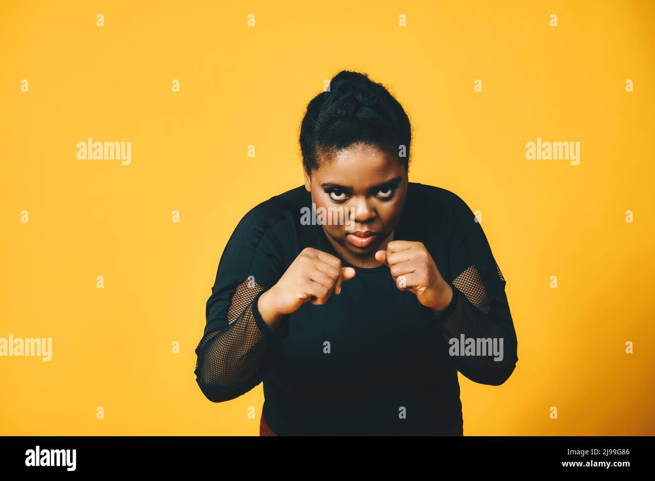 Porträt der schwarzen Frau mit Armen in Kampfposition auf gelbem Hintergrund Studio Stockfoto