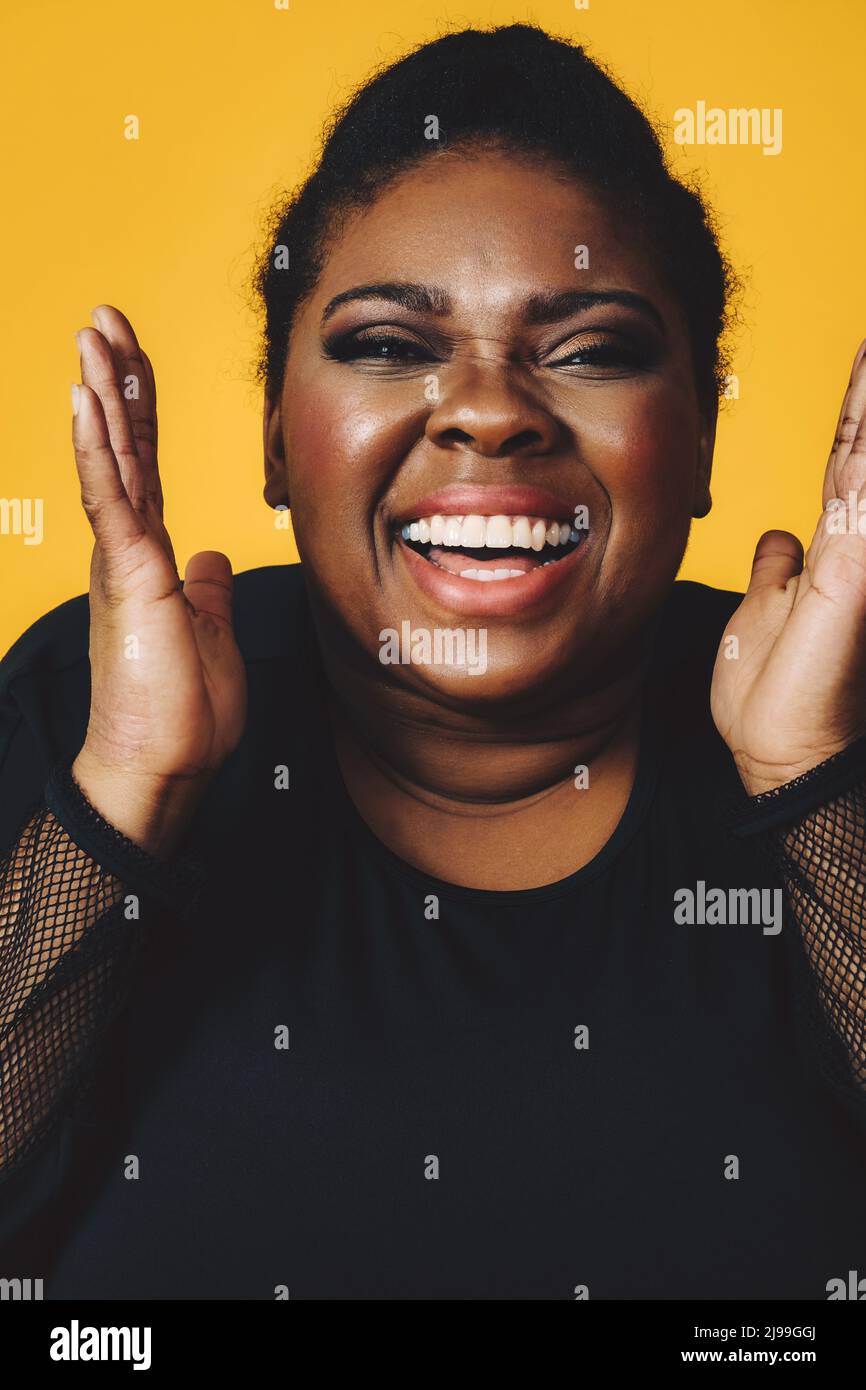 Nahaufnahme Porträt einer jungen erwachsenen schwarzen Frau in lachend mit Mund offen toothy Lächeln auf gelbem Hintergrund Studio Stockfoto