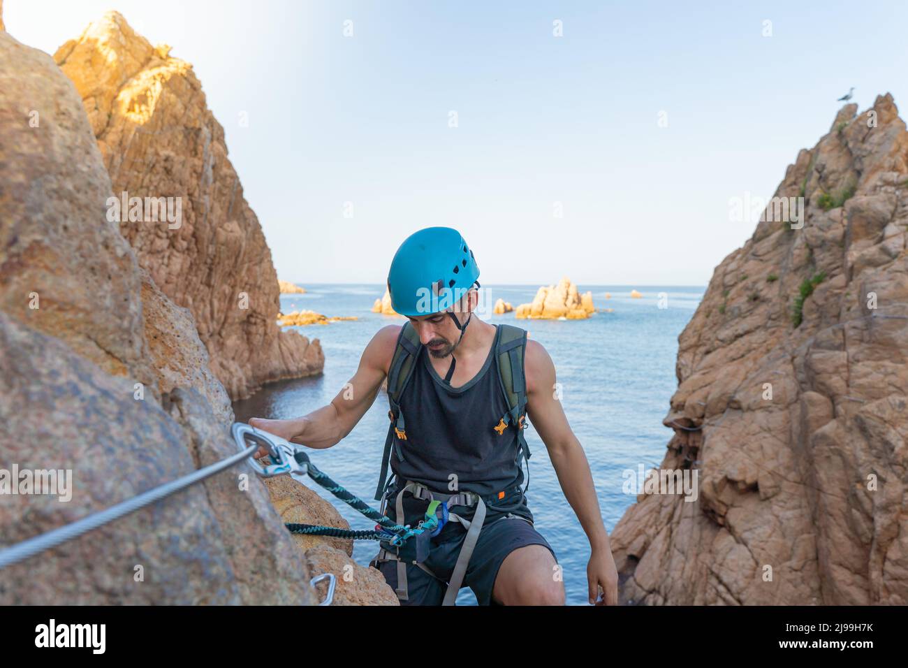 Junger Bergsteiger starker Erfolg beim Wandern auf Felsen über dem Meer mit Seil und Helm. Stockfoto