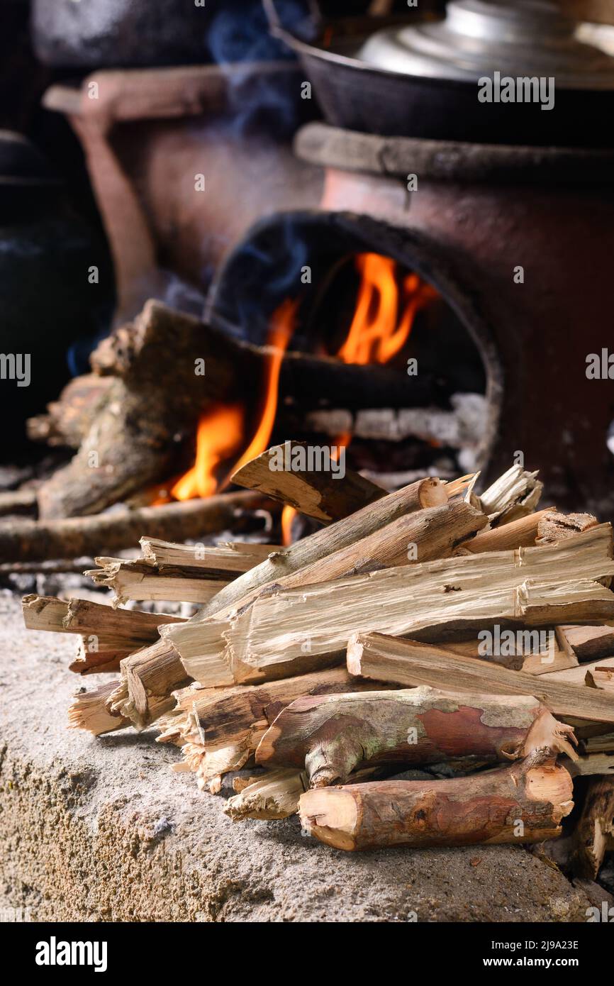 Gesammeltes, gehacktes Brennholz zum Kochen, Feuerflammen und Tonofen mit Töpfen im Hintergrund, traditionelle Küche und einfacher Lebensstil Stockfoto